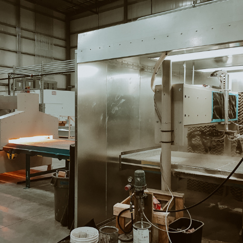A large spray booth with an industrial conveyor system running through automatic spray system and then an oven.